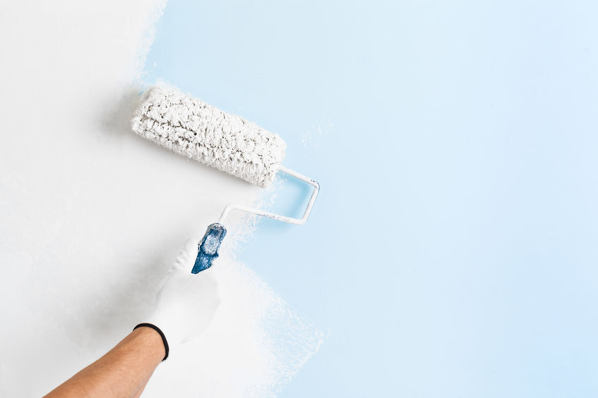 Close up of painter hand in white glove painting a wall with paint roller; copy space